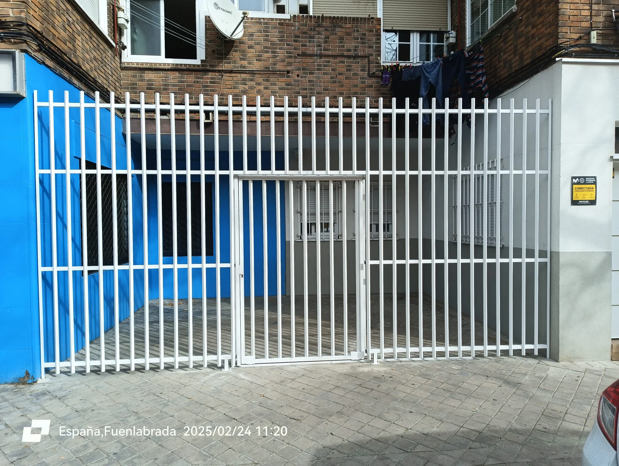 Cerramiento de reja metálica blanca con puerta peatonal abatible en patio de comunidad en Fuenlabrada